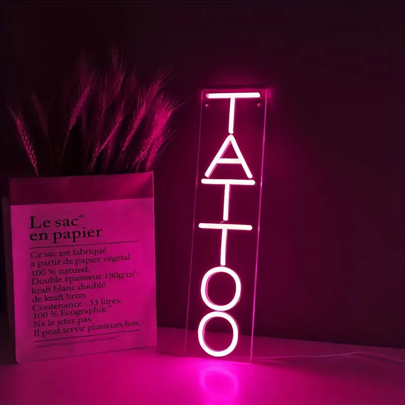 Pink neon sign reading TATTOO, with paper bag and floral decor