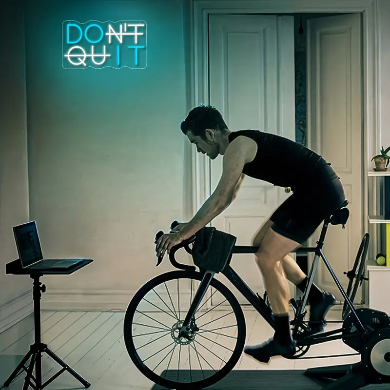 Man cycling indoors under neon Don't Quit sign, training