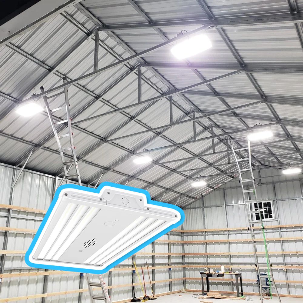 A close-up of a white LED high bay light fixture, with a background showing several of the same lights installed and illuminating a large metal workshop with a high steel-truss ceiling