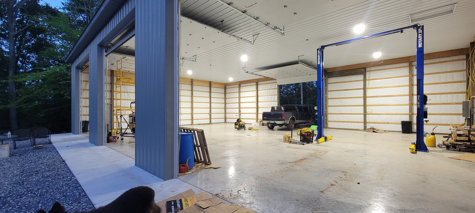 Bright LED shop light fixtures illuminate a spacious garage interior featuring a blue vehicle lift and truck.
