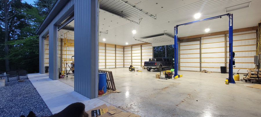 Bright LED shop light fixtures illuminate a spacious garage interior featuring a blue vehicle lift and truck.