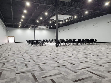 A large, empty event hall with modern lighting and banquet tables set up in the distance.