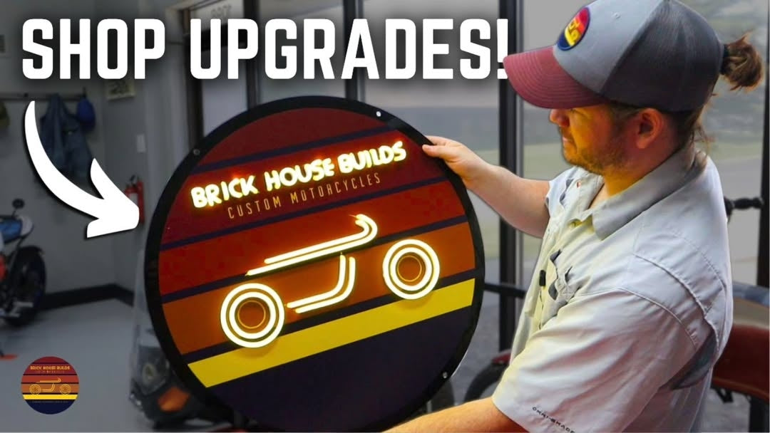 A man holding a new, circular lighted sign for his shop, 'Brick House Builds Custom Motorcycles'. The image text, 'Shop Upgrades!', indicates the sign is a new addition to the business.