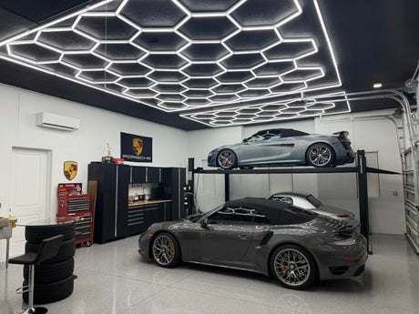 Modern garage with sleek hexagonal LED ceiling lights, featuring two luxury cars on a lift and organized storage.
