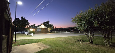 LED parking lot lights illuminate a quiet rural area at dusk, highlighting a barn and fenced yard.