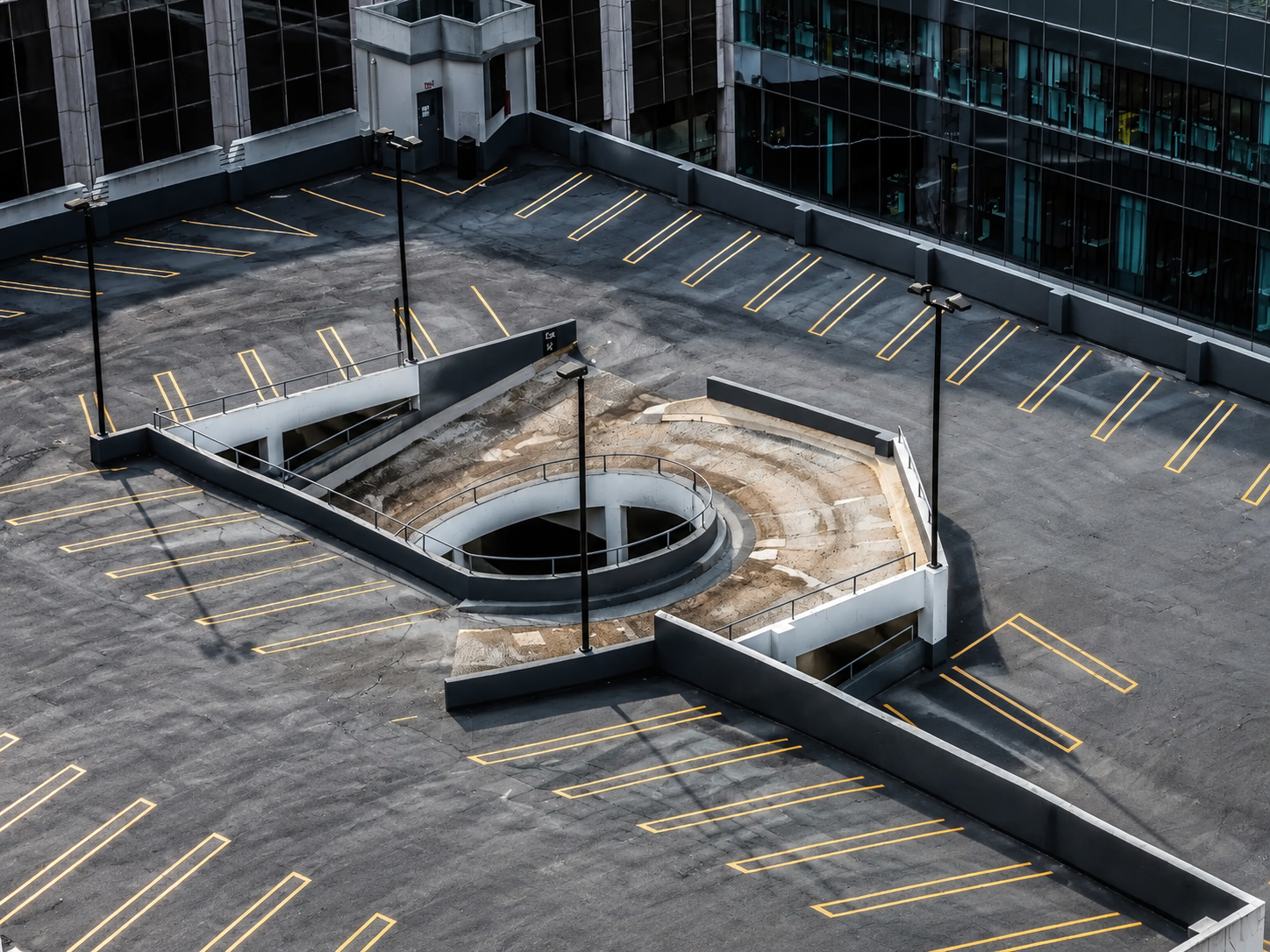 Aerial view of a commercial parking garage rooftop with marked parking spaces and access ramps to lower levels