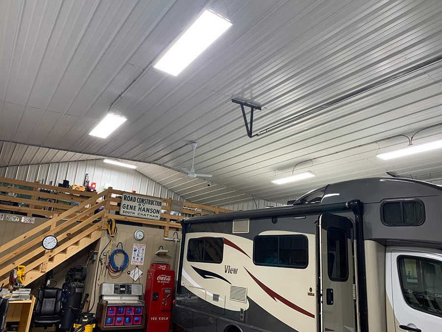 the interior of a spacious garage or workshop with an RV parked inside, featuring bright overhead lights