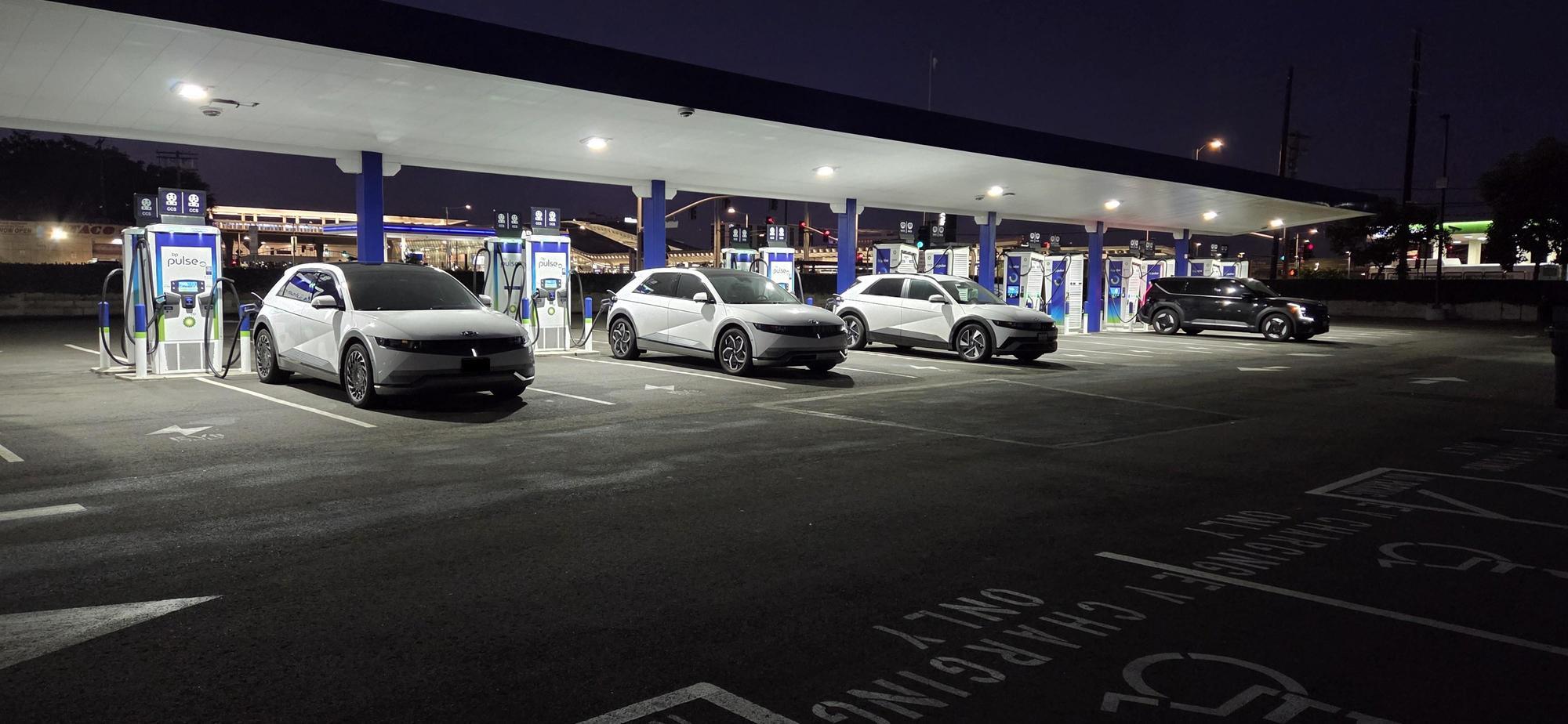Covered EV charging canopy with rows of chargers and white electric cars under bright LED parking lot lights