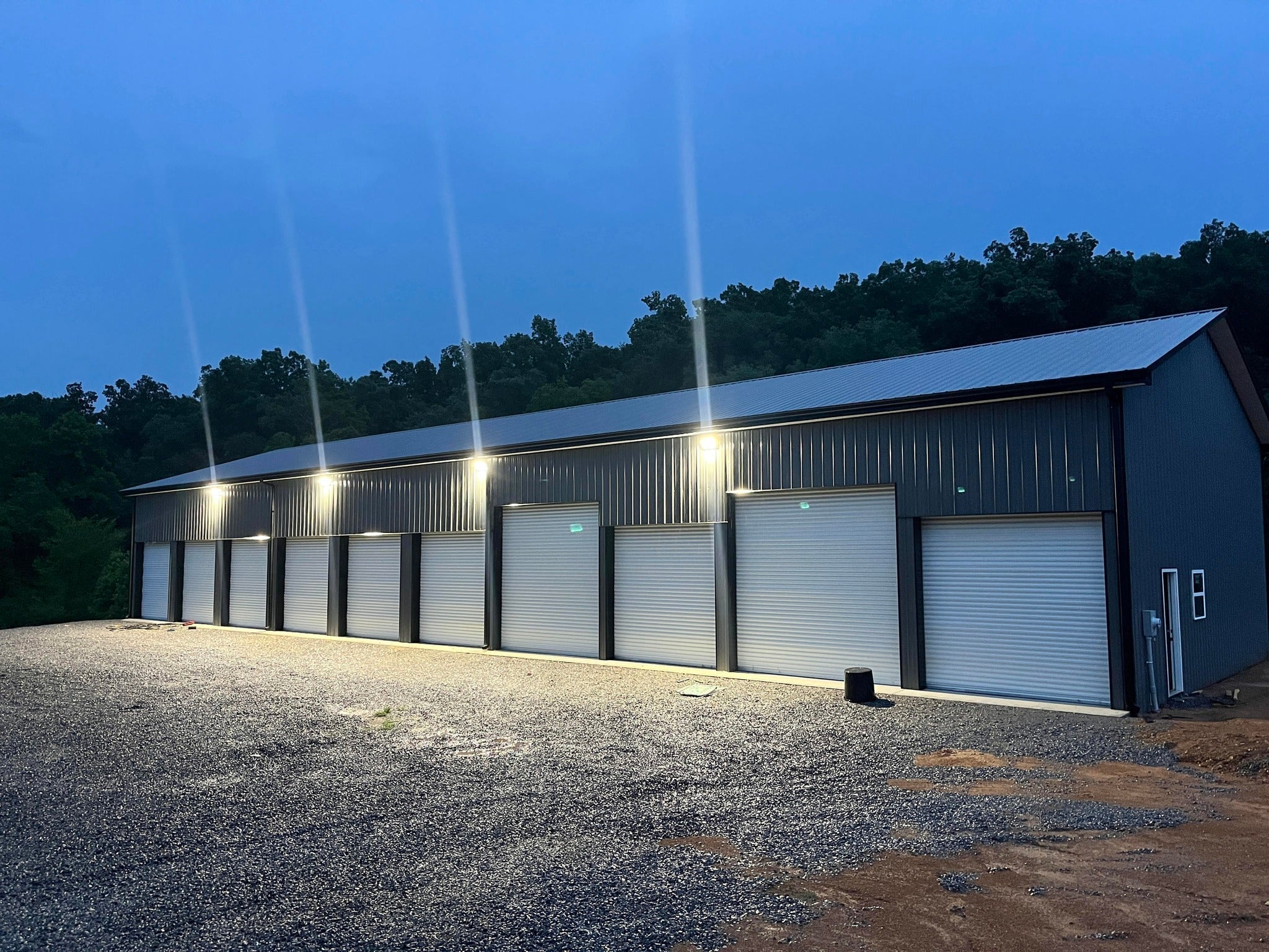 Outdoor LED flood lights illuminating a commercial metal warehouse building with roll-up doors at night