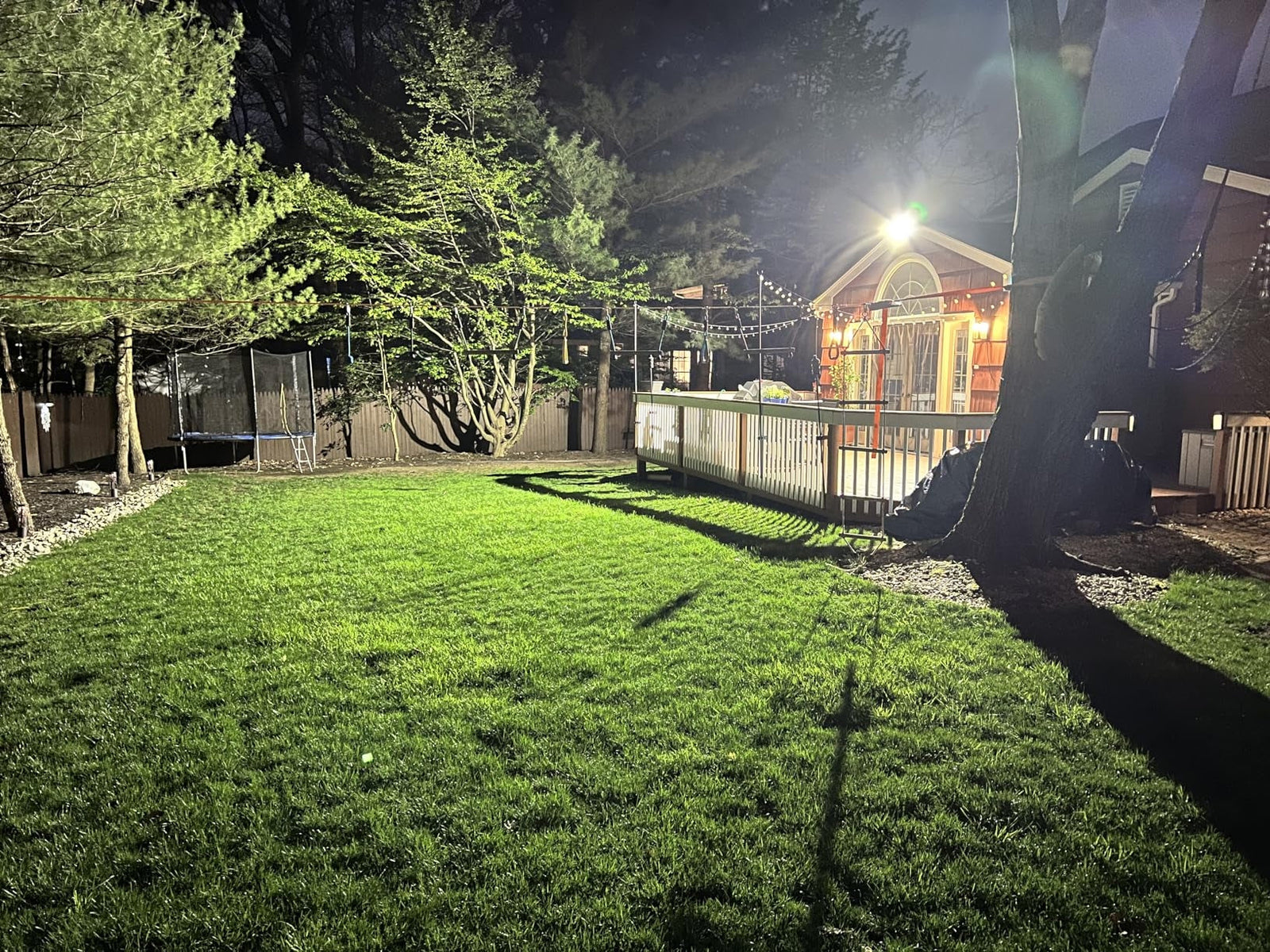 Bright outdoor LED security light installed on a house illuminating a residential backyard lawn and wooden deck area.