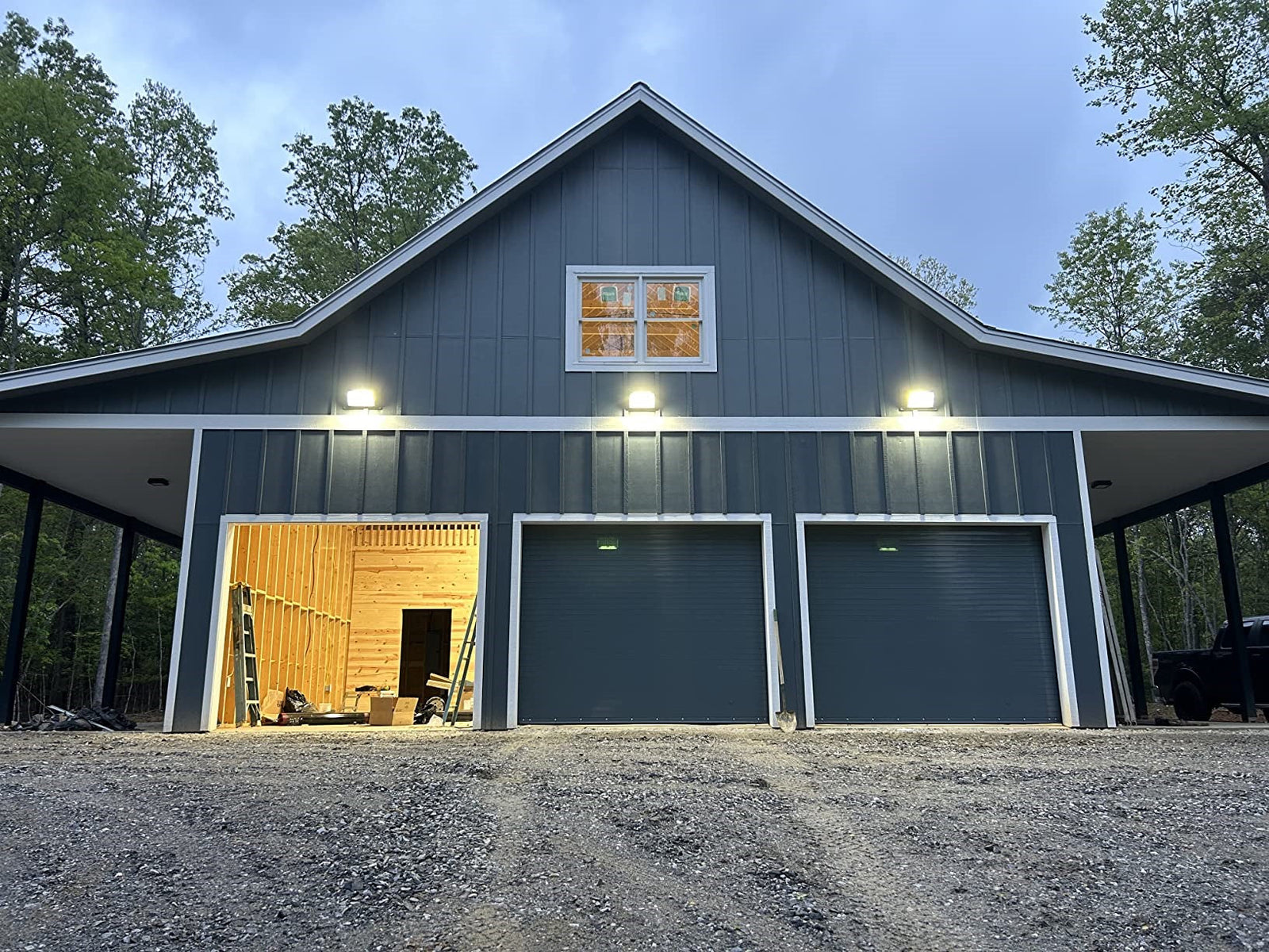 Three LED wall pack lights mounted above garage doors on a blue barn at twilight.