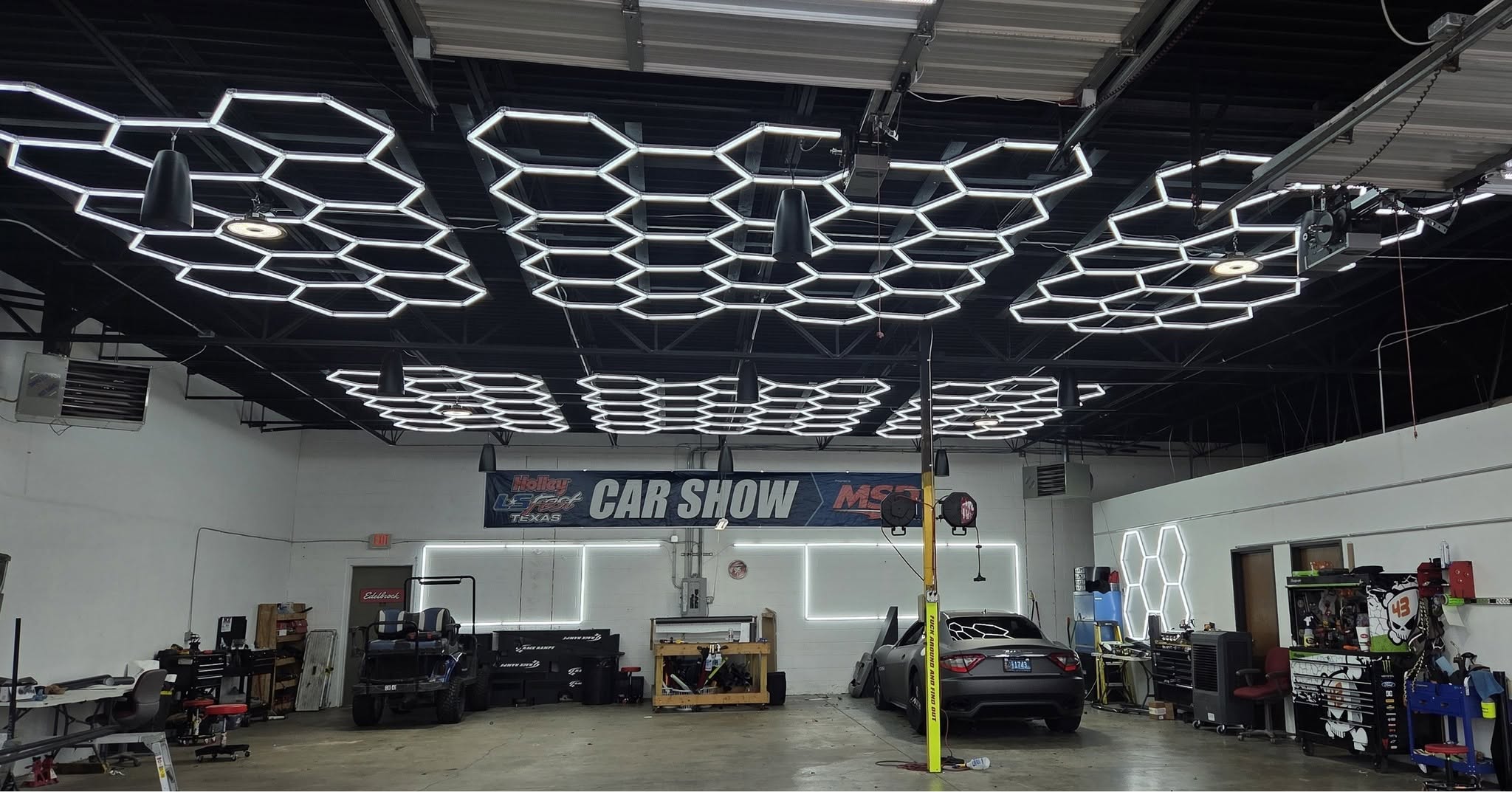 High workshop ceiling filled with hexagon garage lights above a sports car on a lift and work benches
