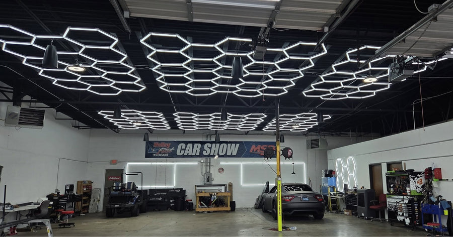 High workshop ceiling filled with hexagon garage lights above a sports car on a lift and work benches