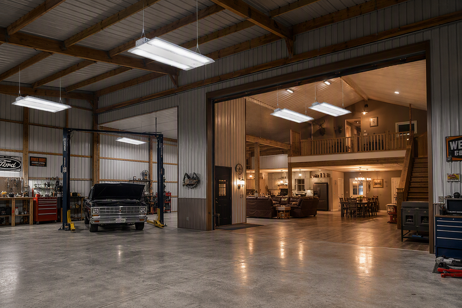 LED high-bay fixtures illuminate a tall pole-barn shop beside a warmly lit living area.