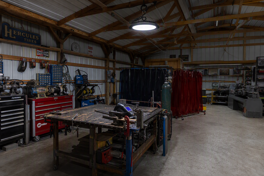 LED high-bay fixture illuminating a tidy home welding and fabrication bay while the welding station remains clear of its direct spark path