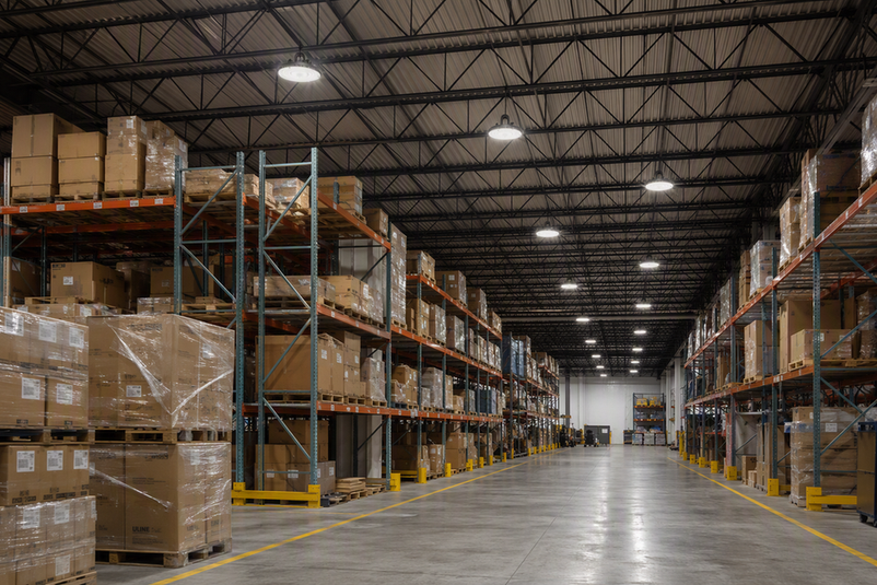 Commercial high bay LED fixtures illuminate a warehouse aisle from the ceiling.