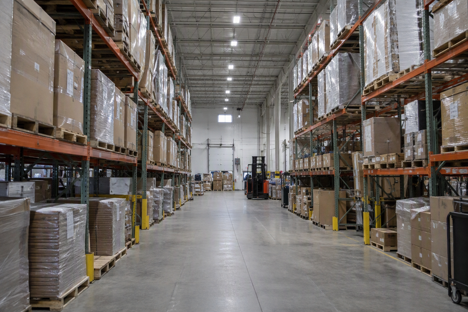 Wide view of a high-ceiling warehouse storage aisle, with existing high-bay lighting and racking that limits access to the work area.