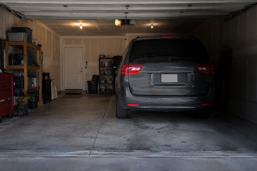 A tall van parked in a deep garage blocks some overhead light, leaving a side work area dim.