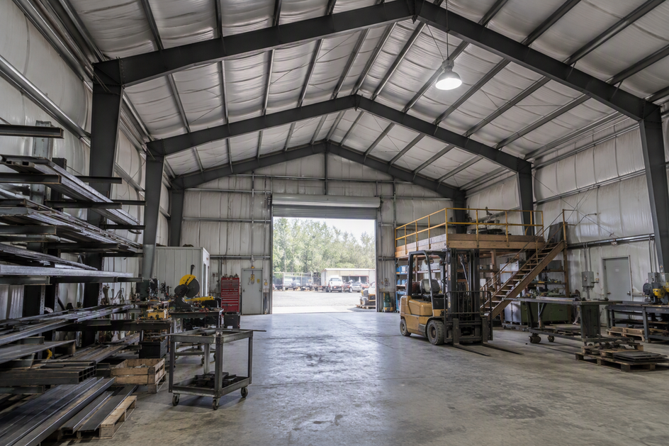 A high-bay fixture beneath a pitched warehouse roof, with exposed trusses and the work area below.