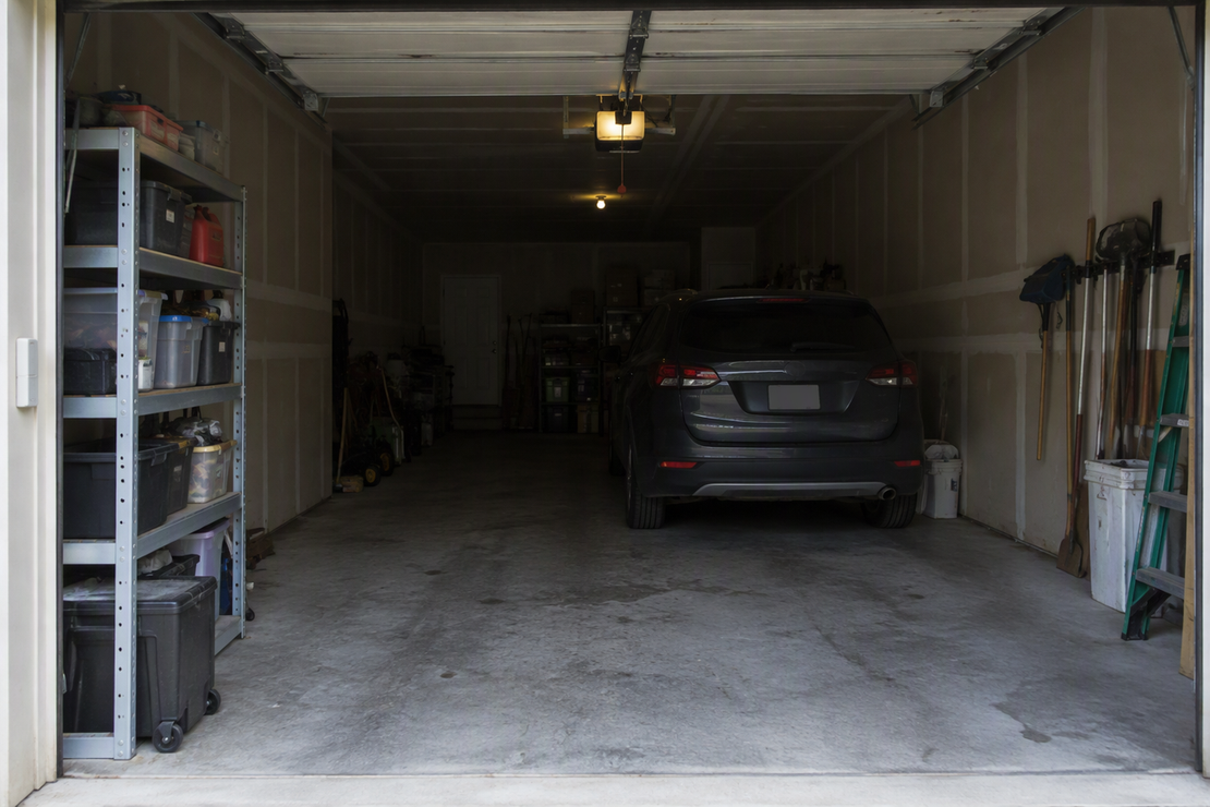 View from the entrance of a deep garage, with the rear work area noticeably dimmer than the front and shelving creating a localized shadow.