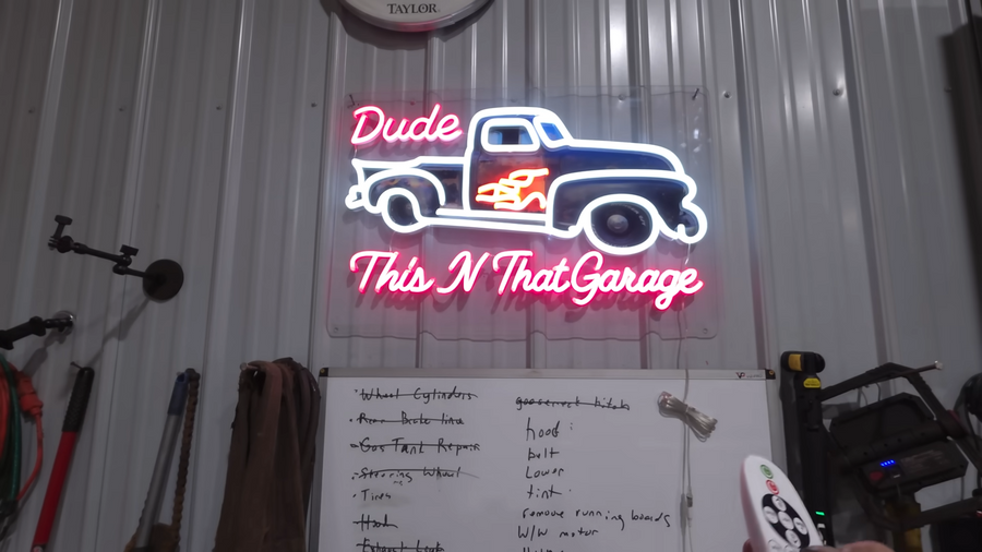 A custom neon garage sign displayed above a workshop whiteboard