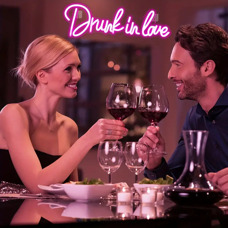 Couple toasting with wine under a "Drunk in Love" neon sign