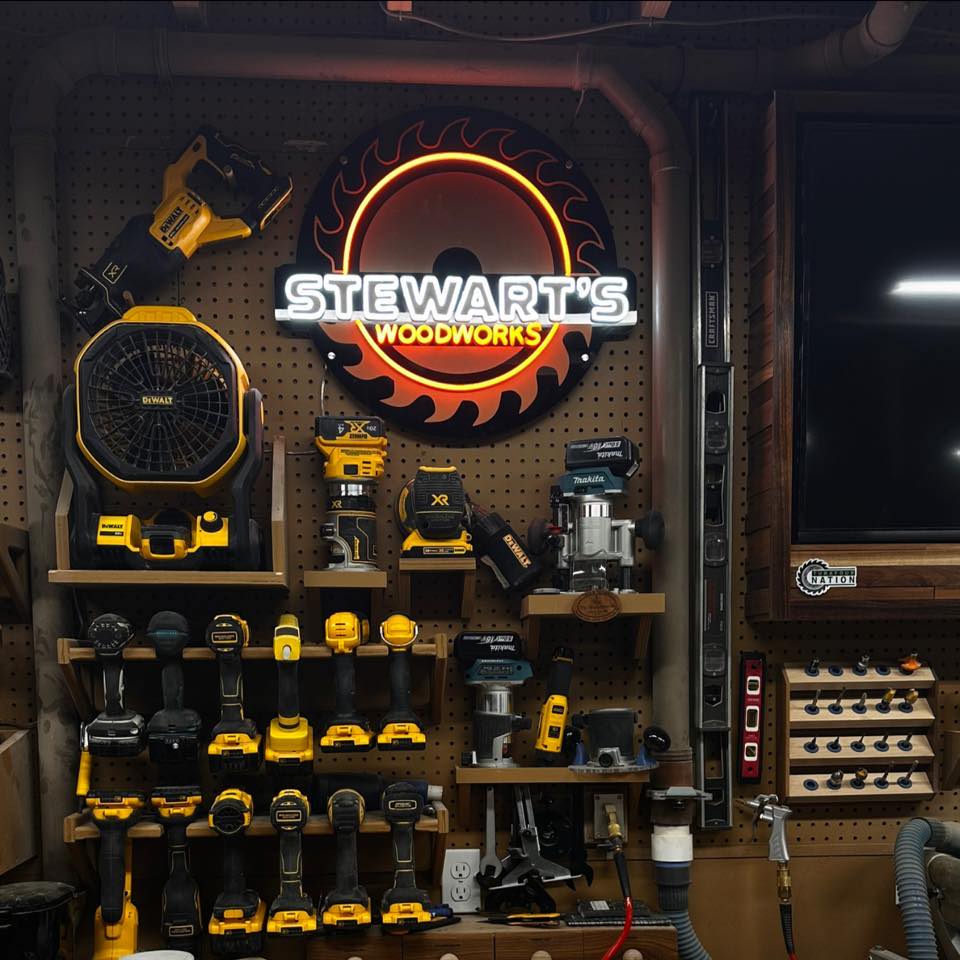 Illuminated saw-blade neon sign above organized DeWalt tools under bright LED shop lights in a garage woodshop