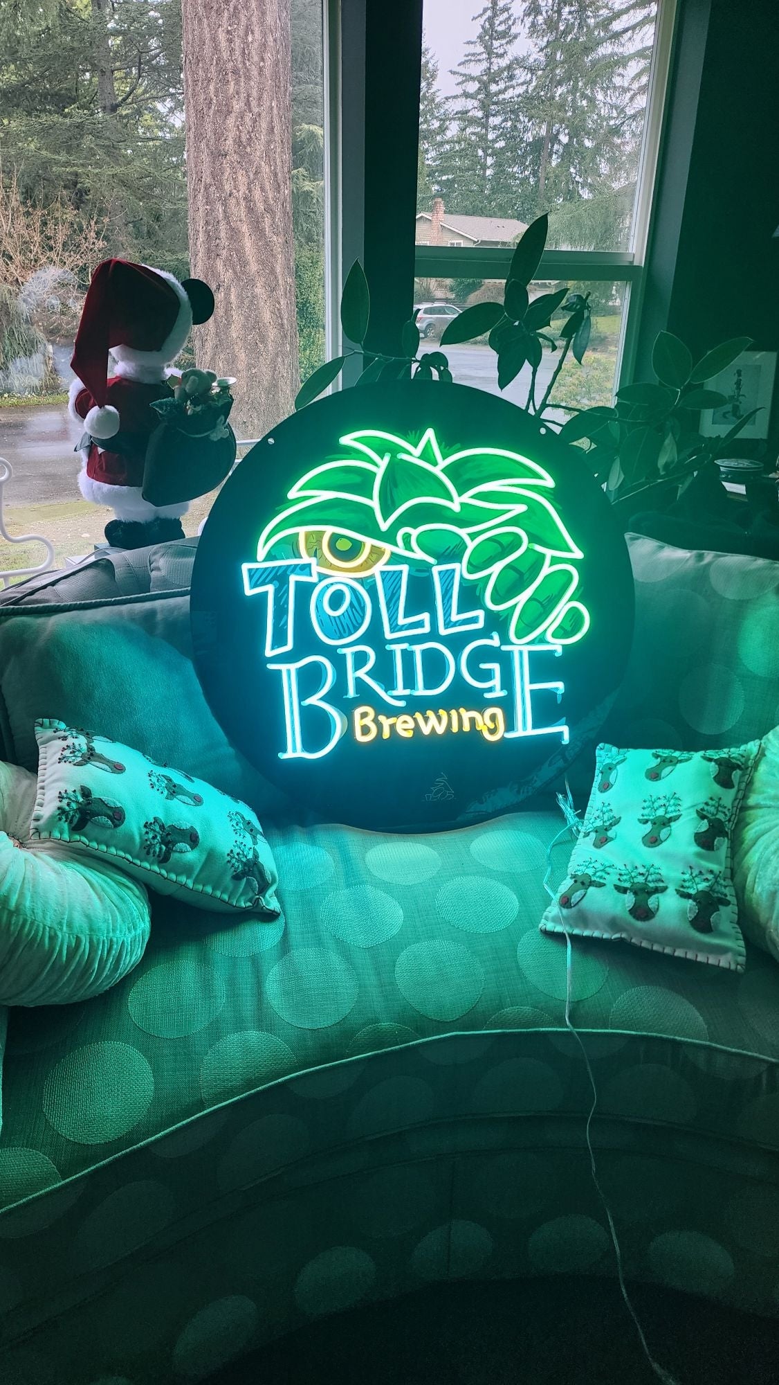 Custom LED neon sign 'Toll Bridge Brewing' glowing green on a sofa