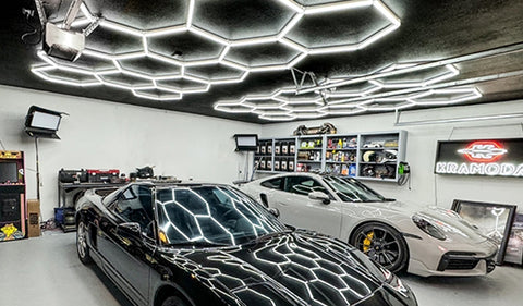 Two-car garage converted to a workshop with modular LED hexagon lights mounted to the ceiling and red perimeter accent lighting; bright, even task lighting ideal for home shop, garage gym, or hobby workspace; visible garage door openers and bicycles show a residential installation.