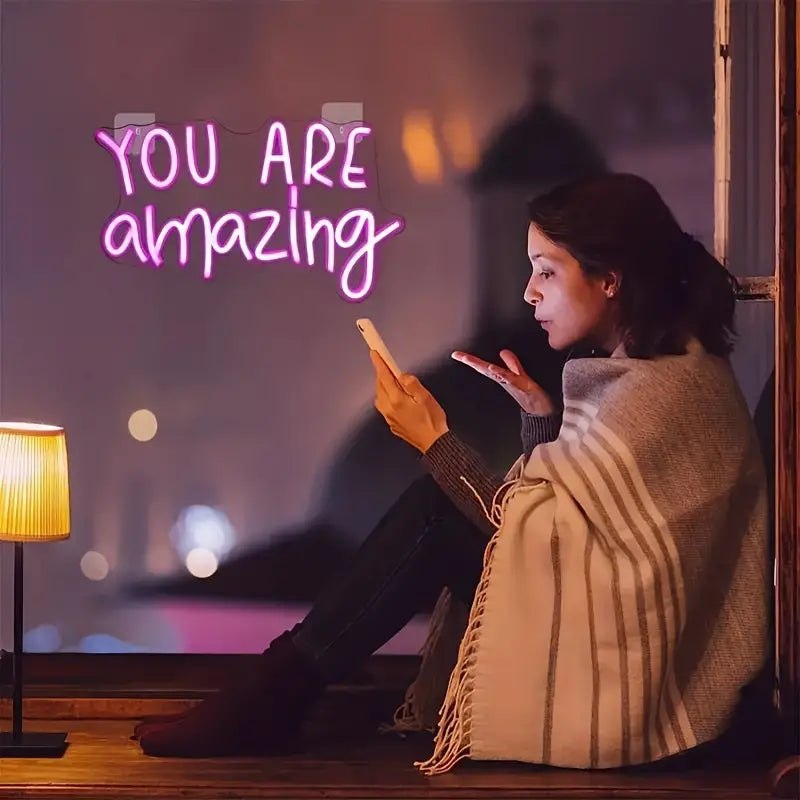 Woman using phone under You Are Amazing neon light